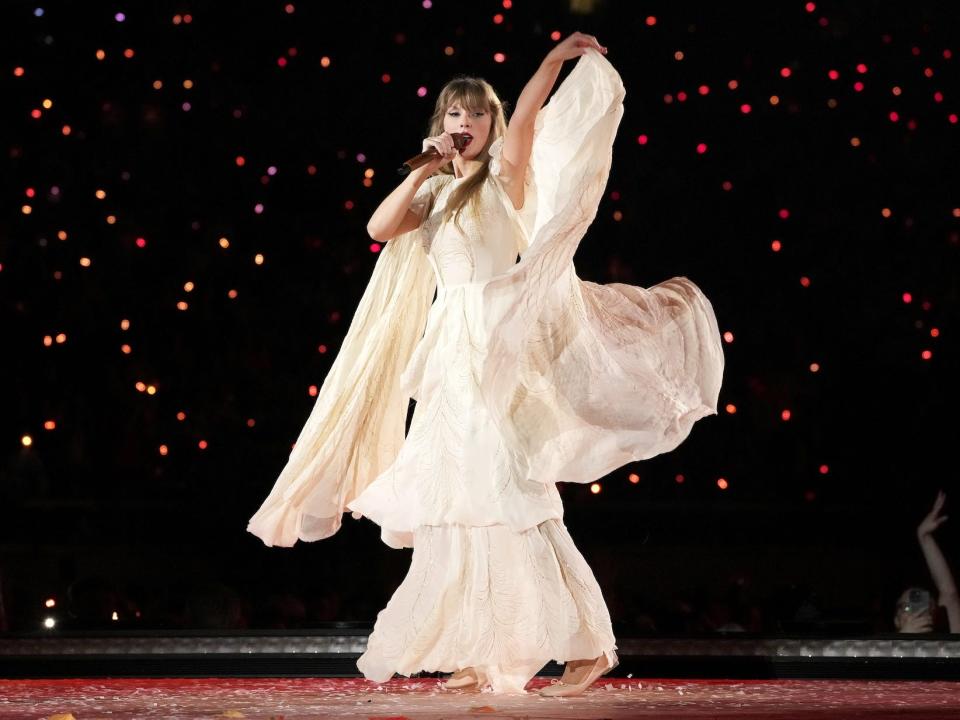 Taylor Swift performs in a white dress.