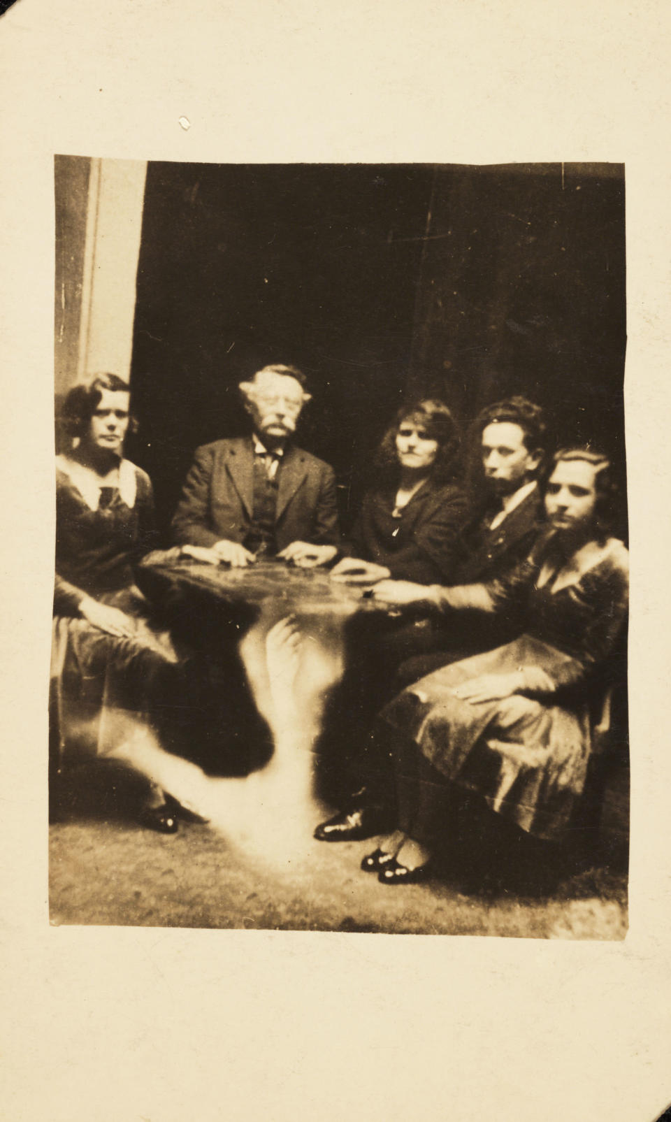 A photograph of a group gathered at a seance, taken by William Hope (1863-1933). The information accompanying the spirit album states that the table is levitating - in reality the image of a ghostly arm has been superimposed over the table-stand through double exposure. Hope's spirit album photographs use multiple exposure techniques to render the appearance of ghostly apparitions. Hope founded the spiritualist society known as the Crewe Circle and his work was popular after World War One when many bereaved people were desperate to find evidence of loved ones living beyond the grave. Although his deception was publicly exposed by a private investigator in 1922, he continued to practice. (Photo by SSPL/Getty Images)