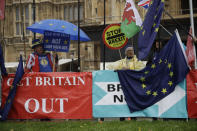 Anti-Brexit remain in the European Union supporter Steve Bray, left, protests next to banners placed by pro-Brexit leave the EU supporters backdropped by the Houses of Parliament in London, Thursday, Oct. 24, 2019. Britain's Prime Minister Boris Johnson won Parliament's backing for his exit deal on Wednesday, but then lost a key vote on its timing, effectively guaranteeing that Brexit won't happen on the scheduled date of Oct. 31. (AP Photo/Matt Dunham)