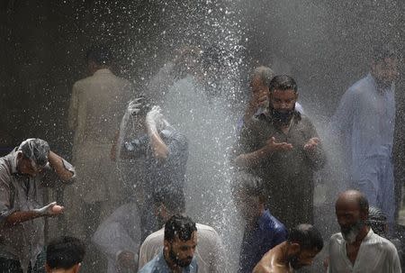 People are seen bathing while others cool off from the heat as they are sprayed with water jetting out from a leaking water pipeline in Karachi, Pakistan, June 25, 2015. REUTERS/Akhtar Soomro