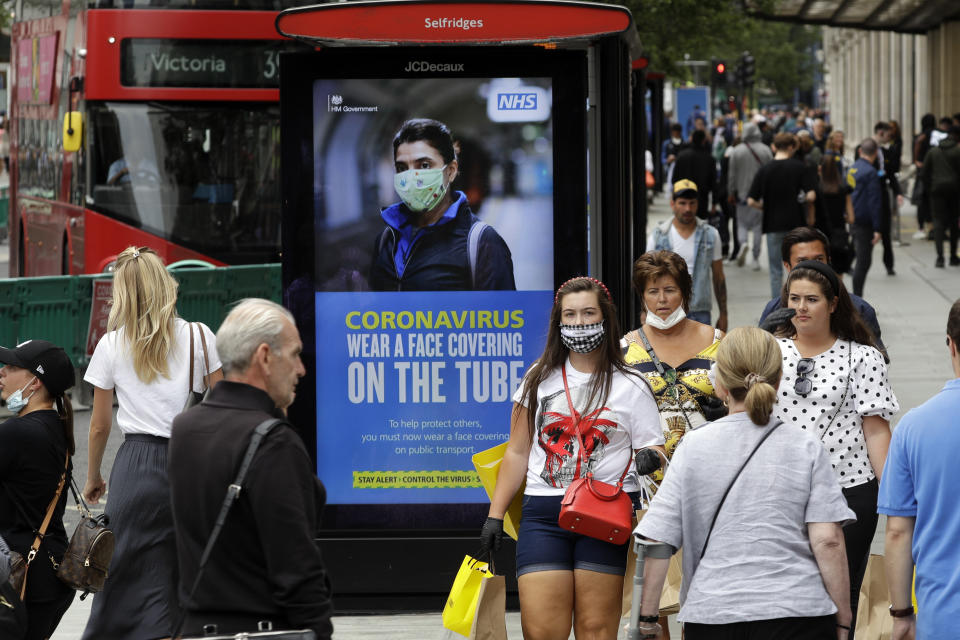 People walk by a COVID-19 infection awareness poster in London, Monday, June 15, 2020. After three months of being closed under coronavirus restrictions, shops selling fashion, toys and other non-essential goods are being allowed to reopen across England for the first time since the country went into lockdown in March.(AP Photo/Matt Dunham)