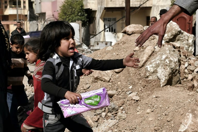 An Iraqi girl is helped by a man during aid distribution in western Mosul