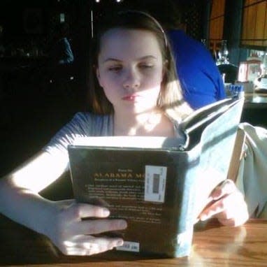 Alex Garner reading a book at age 11. Her mom often called her a bookworm, as she rarely traveled without one. The archival photo is a bit blurry, so it's difficult to identify the book, but the shades and table are clearly from a Cracker Barrel.