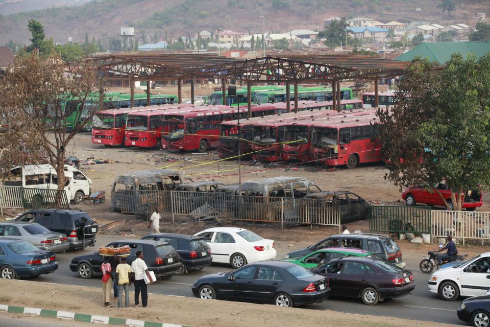 Cars drive past as onlookers inspect the scene of an explosion at a bus park in Abuja, Nigeria, Tuesday, April. 15, 2014, with at least 72 feared dead as the blast destroyed more than 30 vehicles and caused secondary explosions as their fuel tanks exploded and burned. The attack just miles from Nigeria's seat of government increases doubts about the military's ability to contain an Islamic uprising that is dividing the country on religious lines as never before. (AP Photo/ Sunday Alamba)