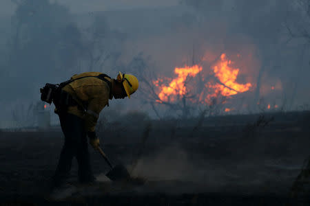 A firefighter works to put out hot spots on a fast moving wind driven wildfire in Orange, California, U.S., October 9, 2017. REUTERS/Mike Blake