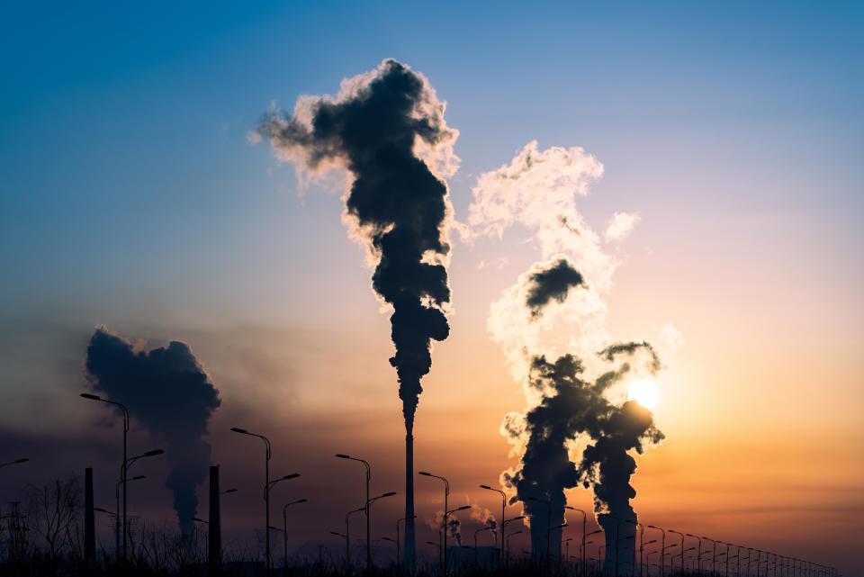 Thick, dark smoke rises from chimneys in front of a clear sky with bright sunshine 