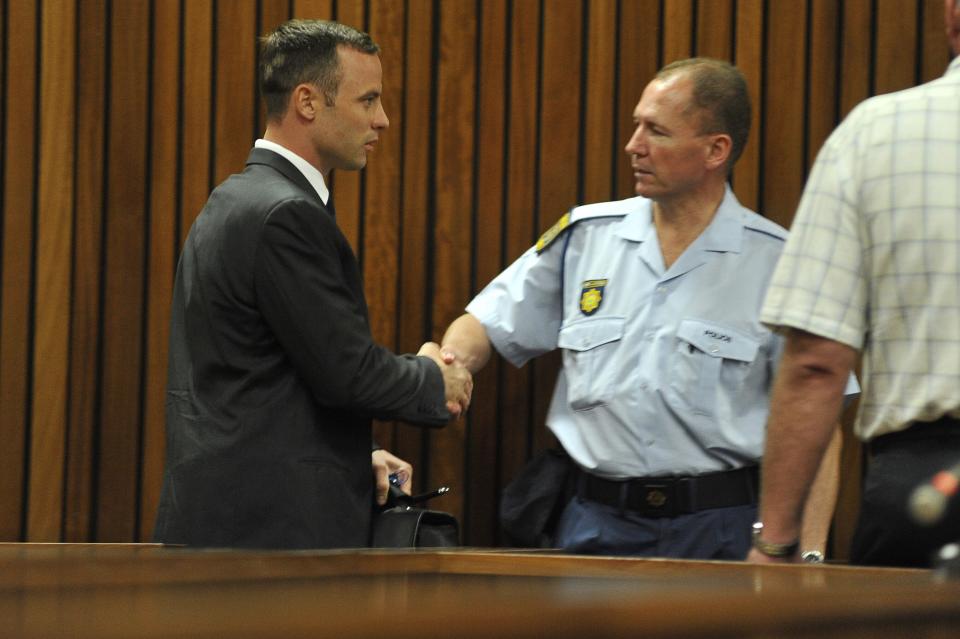Olympic and Paralympic track star Oscar Pistorius (L) greets a policeman as he makes his way to the dock in the North Gauteng High Court in Pretoria March 24, 2014. The track star, nicknamed the "Blade Runner", is on trial for murdering his girlfriend Reeva Steenkamp at his suburban Pretoria home on Valentine's Day last year. REUTERS/Ihsaan Haffejee/Pool (SOUTH AFRICA - Tags: SPORT CRIME LAW ATHLETICS)