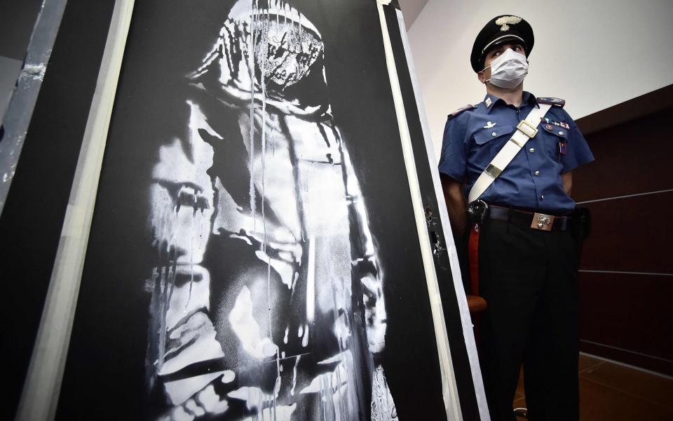 A policeman stands guard near a piece of art attributed to Banksy, that was stolen at the Bataclan in Paris in 2019, and found in Italy - AFP