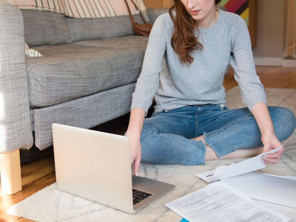 woman sitting on living room floor organizes finances and uses computer