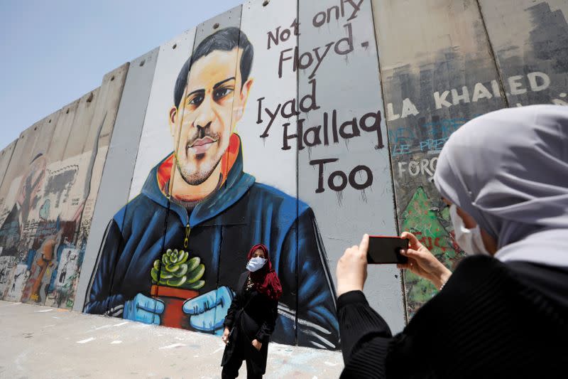 A Palestinian woman takes pictures of her friend posing in front of the Israeli barrier with a mural depicting Iyad al-Halaq, in Bethlehem in the Israeli-occupied West Bank