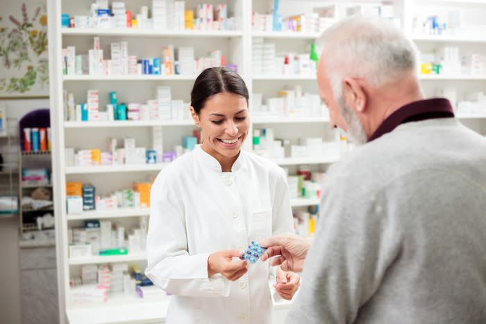 A female pharmacist dispensing medicine to an older man.