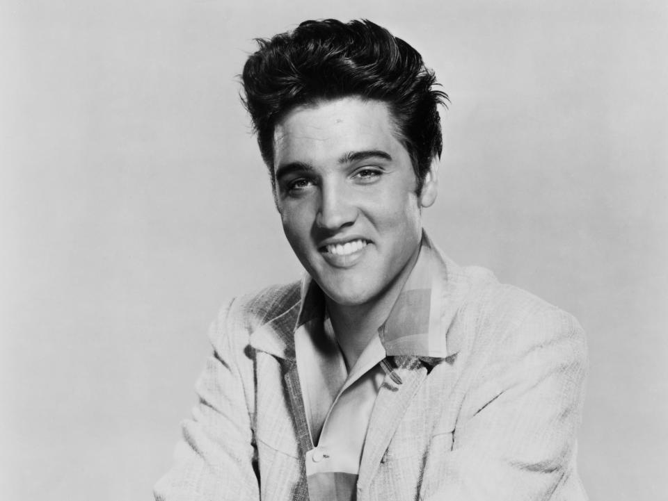 circa 1955: A portrait of American rock musician Elvis Presley (1935 - 1977) seated with his arms crossed on top of a guitar turned downwards on his lap. (