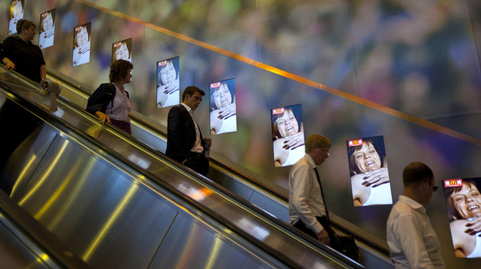 In this Tuesday, July 24, 2012 photo, Londoners observe electronic advertising by one of the Olympic sponsors, as they pass through an underground tube station, ahead of the 2012 Summer Olympics, in London. (AP Photo/Ben Curtis)