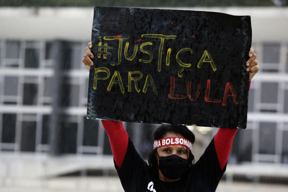 A demonstrator wearing a mask to curb the spread of the new coronavirus and wearing a headband with text in Portuguese that reads "Bolsonaro out" raises a sign that reads "Justice for Lula," in reference to former Brazilian President Luiz Inacio Lula da Silva, during protest commemorating the Supreme Court's decision to suspend proceedings against Lula, in front of the Supreme Court building in Brasilia, Brazil, Monday, March 8, 2021. (AP Photo/Eraldo Peres)