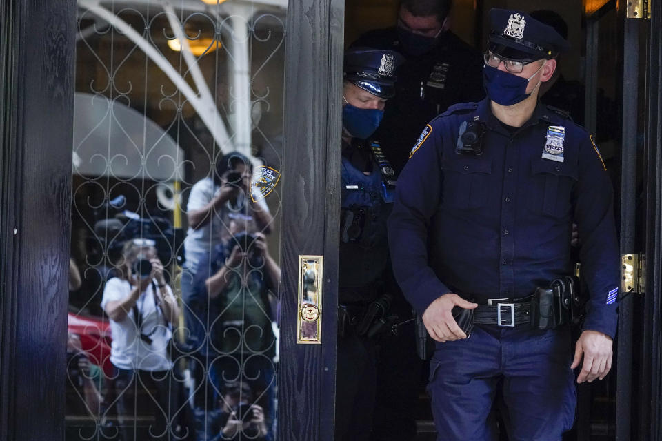 FILE - In this Wednesday, April 28, 2021, file photo, members of the media are reflected in the window of a door as New York City Police officers walk out of the apartment building where former New York Mayor Rudy Giuliani resides, in New York. Giuliani and his lawyers will get to designate which materials seized from him will be reviewed by a court-appointed expert reviewer to determine what should never be seen by federal prosecutors. As part of the investigation, federal agents seized 18 electronic devices from Giuliani's residence and his firm, Giuliani Partners LLC. (AP Photo/Mary Altaffer, File)