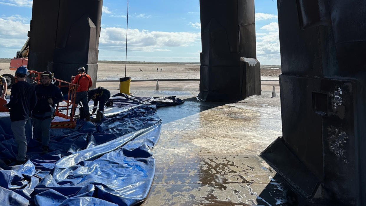  Four workers stand atop a concrete pad surrounded by three large concrete pillars. 