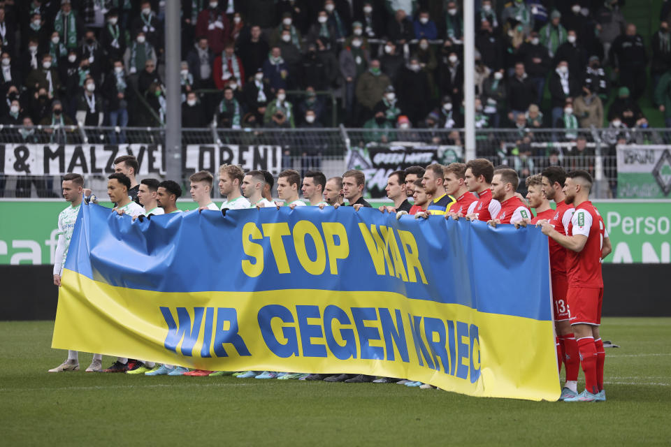 At the start of the match, the players of both teams hold a Ukrainian flag with the inscription "Stop War. We against war." prior the Bundesliga soccer match between Greuther Fuerth and 1. FC Cologne in Fuerth, Germany, Saturday, Feb. 26, 2022. (Daniel Karmann/dpa via AP)