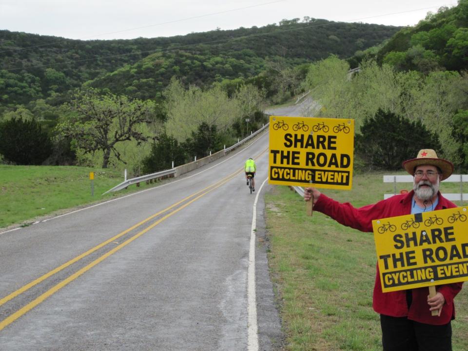 Chandler Otis holds signs on the side of a road in Utopia, Texas, where he and others participated in a Pampered Pedalers cross-country tour in March 2010.