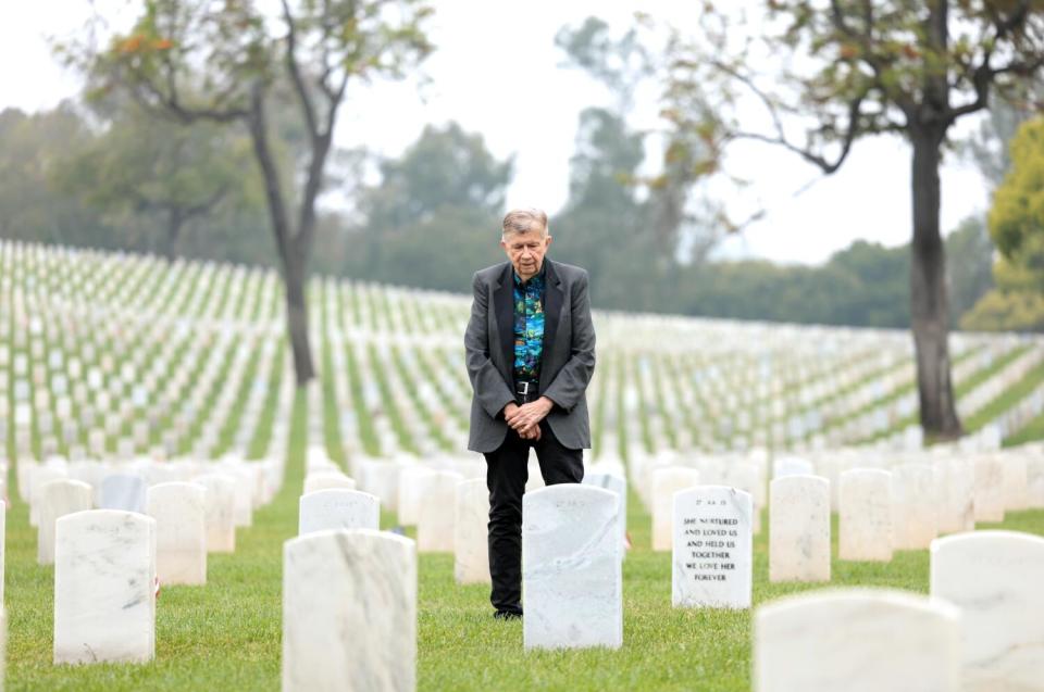 Bob Zaugh stands with hands clasped, looking down at one the uniform white headstones in rows that extend into the distance