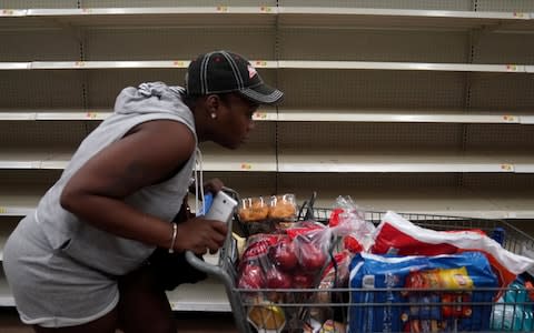 A woman with a full cart walks past empty shelves where bread is normally sold in a Walmart store in advance of Hurricane Irma's expected arrival in North Miami Beach - Credit: CARLO ALLEGRI/Reuters