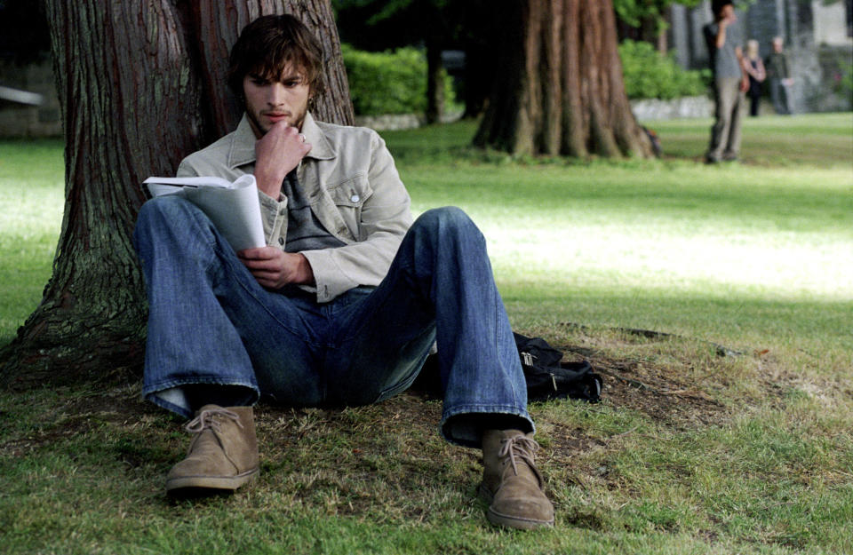 A man sits under a tree, writing in a notebook