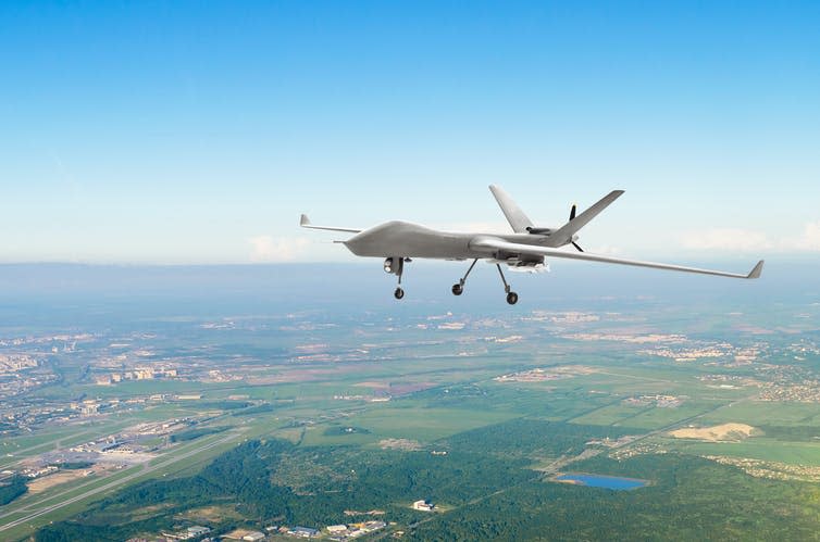 A military drone flying at low altitude over green fields