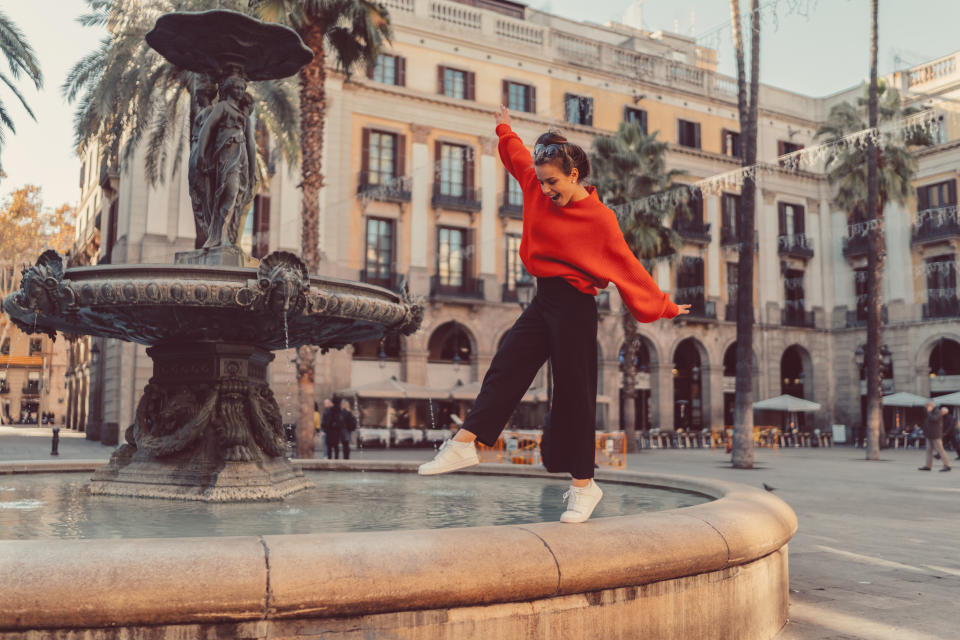 Smiling woman trying to keep balance while walking on one leg at the fountain