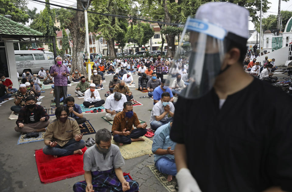 A mosque official in protective gear tasked to take the temperature readings of arriving worshippers, waits at the gate of the Cut Meutia Mosque during a Friday prayer in Jakarta, Indonesia, Friday, June 5, 2020. Muslims in Indonesia's capital held their first communal Friday prayers as mosques closed by the coronavirus outbreak for nine weeks reopened at half capacity. (AP Photo/Dita Alangkara)