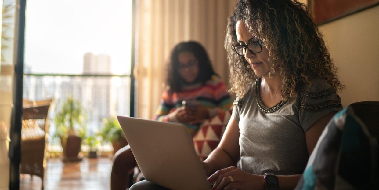 mature woman working at home, using laptop sitting on the couch