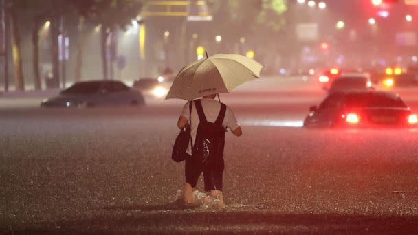 PHOTO: A man wades alongside submerged cars in a street during heavy rainfall in the Gangnam district of Seoul, South Korea, on Aug. 8, 2022. (YONHAP/AFP via Getty Images)