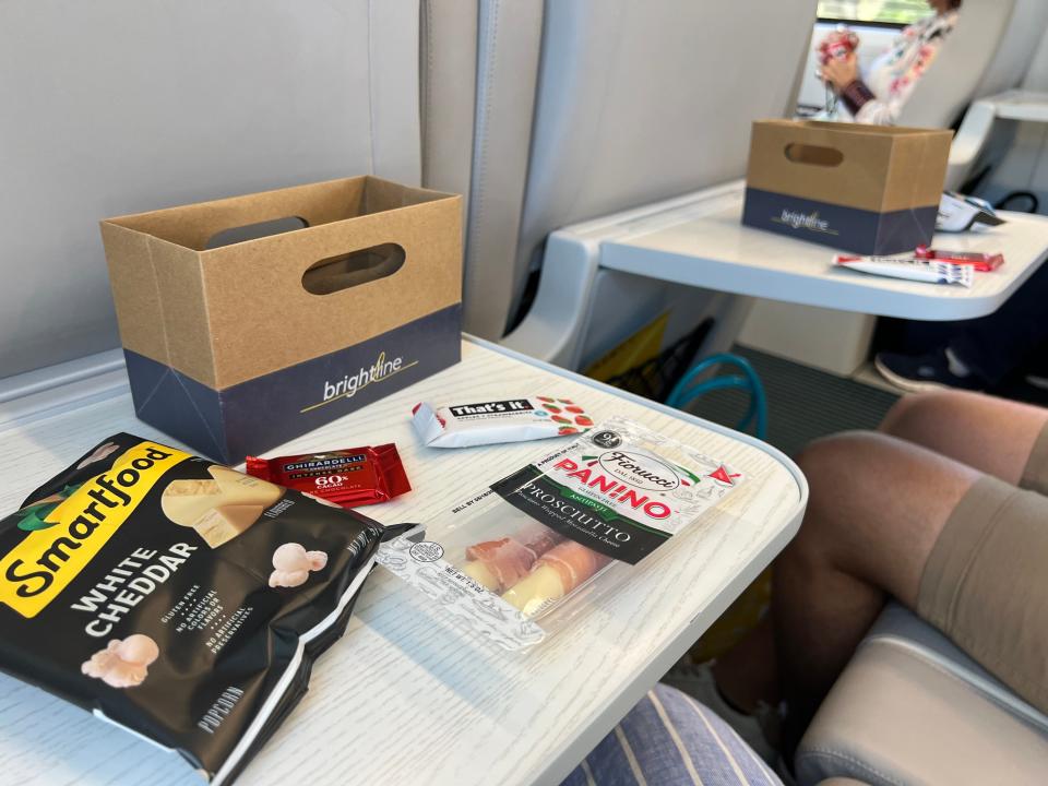 A tray table with snacks including chocolate, popcorn and prosciutto-wrapped cheese are shown.