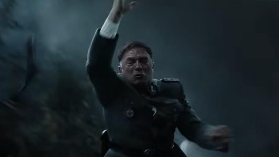 A Nazi officer atop a moving train with his arm up in the air looking pained in Indiana Jones and the Dial of Destiny