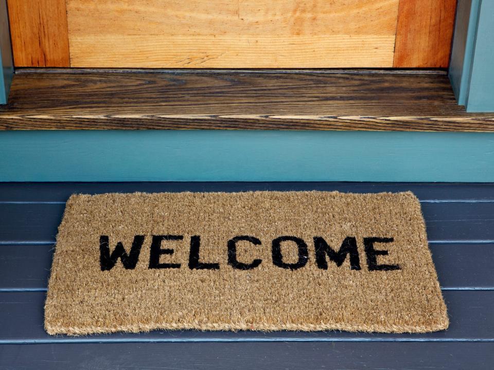 A black deck with a brown "welcome" mat in front of the wooden door, which has a painted blue frame