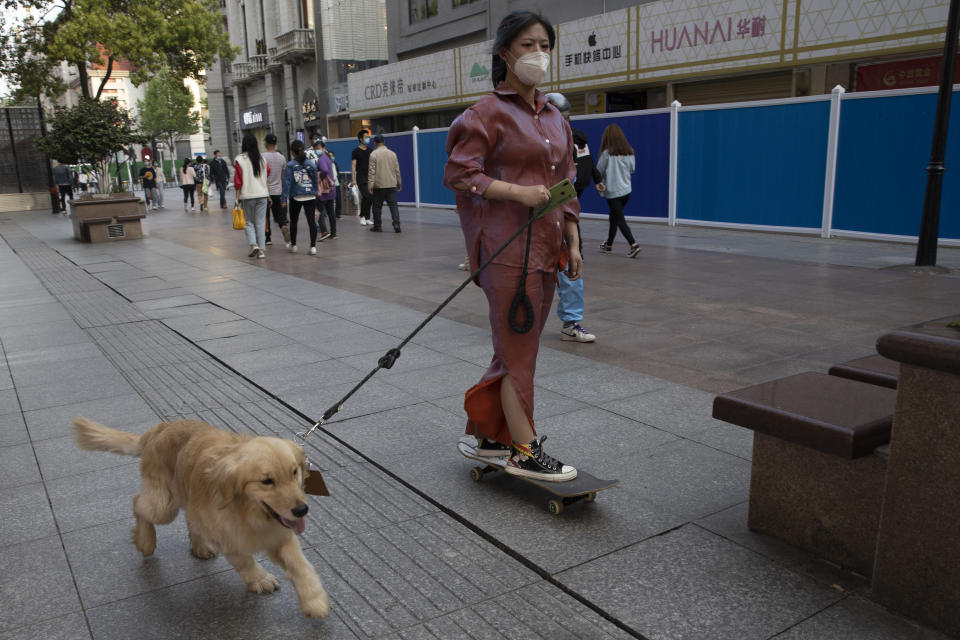 A resident gets a ride from her dog along a retail street in Wuhan in central China's Hubei province, Thursday, April 9, 2020. Released from their apartments after a 2 1/2-month quarantine, residents of the city where the coronavirus pandemic began are cautiously returning to shopping and strolling in the street but say they still go out little and keep children home while they wait for schools to reopen. (AP Photo/Ng Han Guan)