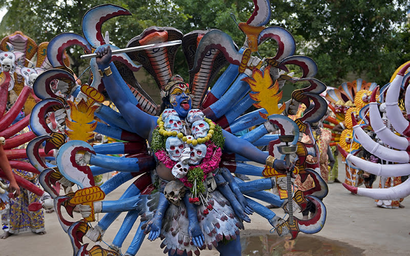 An artist dressed as Hindu goddess Mahakali performs, wearing blue face paint and a costume with many blue arms and hands holding prop curved knives