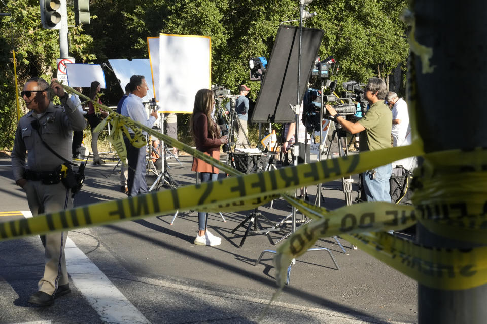 Members of the media broadcast live television coverage behind yellow tapes at the scene of a mass shooting at Cook's Corner, Thursday, Aug. 24, 2023, in Trabuco Canyon, Calif. (AP Photo/Damian Dovarganes)