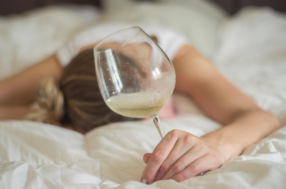 Great concept of alcohol abuse. Young woman, blond hair, fainted in bed after drinking too much alcohol. Glass of wine in hand, bottle of wine.