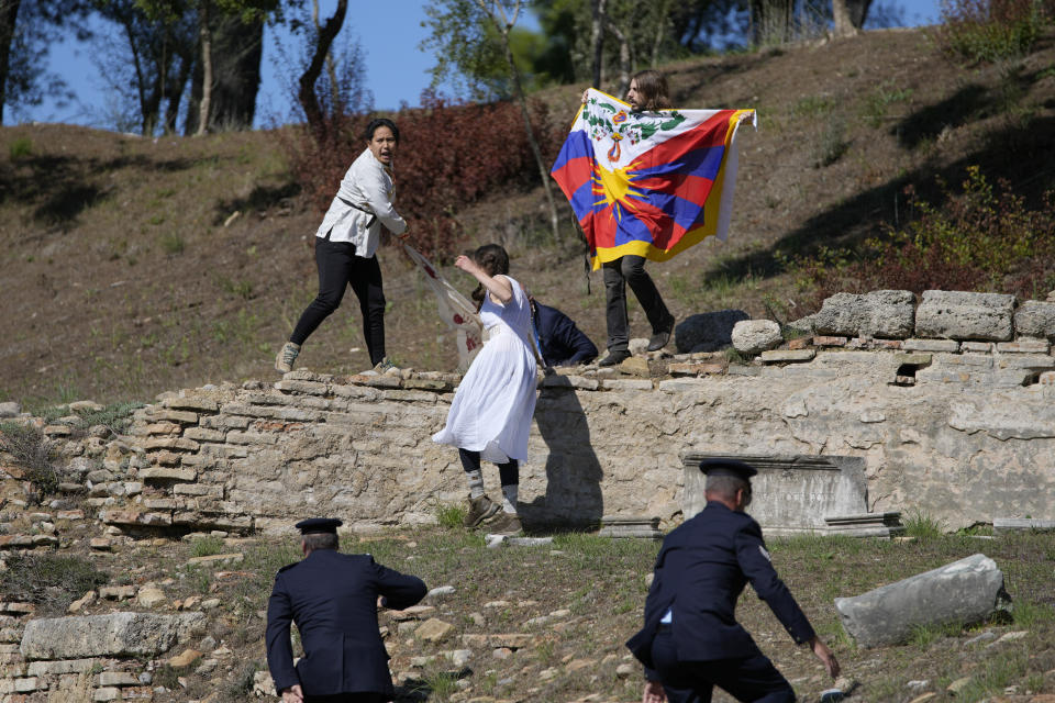 Police officers run to detain protesters displaying a Tibetan flag and a banner disrupting the lighting of the Olympic flame at Ancient Olympia site, birthplace of the ancient Olympics in southwestern Greece, Monday, Oct. 18, 2021. The flame will be transported by torch relay to Beijing, China, which will host the Feb. 4-20, 2022 Winter Olympics. (AP Photo/Thanassis Stavrakis)