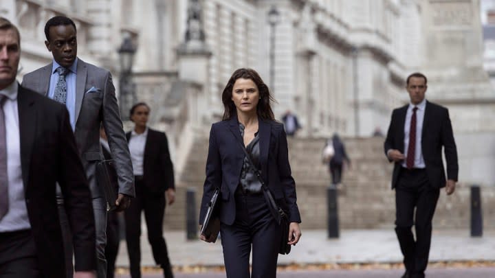 Kate walking down the street, surrounded by others in suits in a scene from The Diplomat on Netflix.