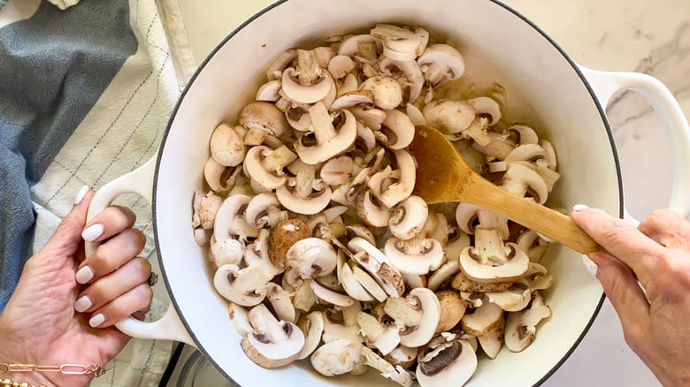 Hands stirring onions and mushrooms in pot