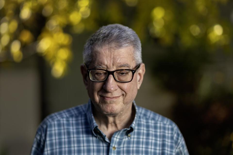 USC professor John Strauss wearing a blue plaid shirt and black glasses with trees in soft focus in the background