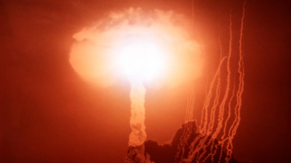 a mushroom cloud from an atom bomb detonation with red sky in the background and trails of smoke