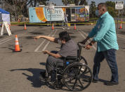 St. John's Well Child and Family Center facilities coordinator Raul Chiriboga, right, helps push cancer survivor Joel Flores, 36, who suffers from autism, to get vaccinated at the COVID-19 vaccination site at the East Los Angeles Civic Center in Los Angeles, Thursday, March 4, 2021. California will begin setting aside 40% of all vaccine doses for the state's most vulnerable neighborhoods in an effort to inoculate people most at risk from the coronavirus more quickly. (AP Photo/Damian Dovarganes)