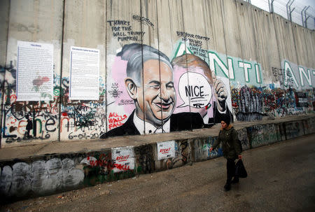 A Palestinian woman walks past a mural depicting Israeli Prime Minister Benjamin Netanyahu that is painted on a part of the Israeli barrier, in the West Bank city of Bethlehem December 6, 2017. REUTERS/Mussa Qawasma