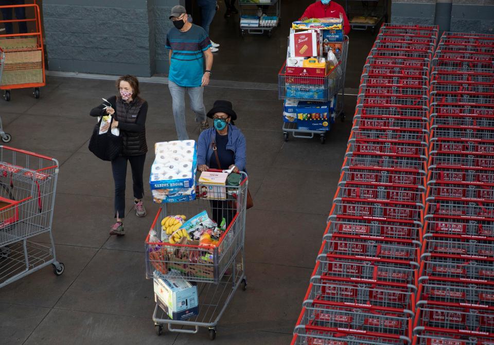 People wearing masks exit a Costco with carts piled high.