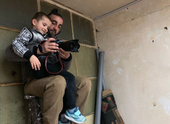 A photographer shows a camera to a kid on his lap.