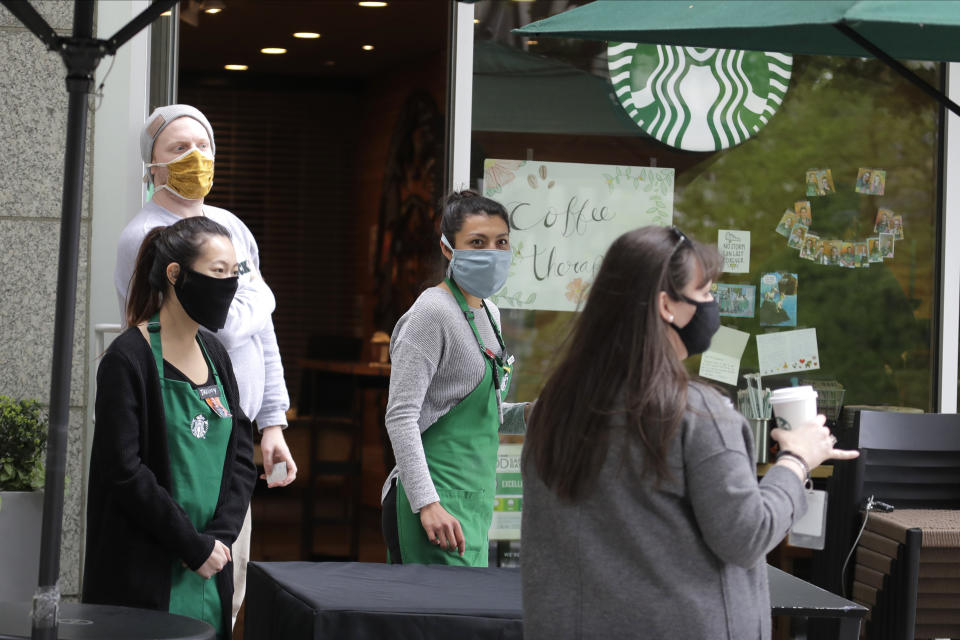 In this May 6, 2020 photo, employees at a Starbucks Coffee store that is open for mobile orders wear masks as they watch a customer leave with an order in downtown Seattle. Nearly all retail stores and restaurants in the area are currently closed or operating under reduced levels of service due to the outbreak of the coronavirus and state-wide stay-at-home orders, which has led to thousands of workers losing their jobs or being furloughed. (AP Photo/Ted S. Warren)