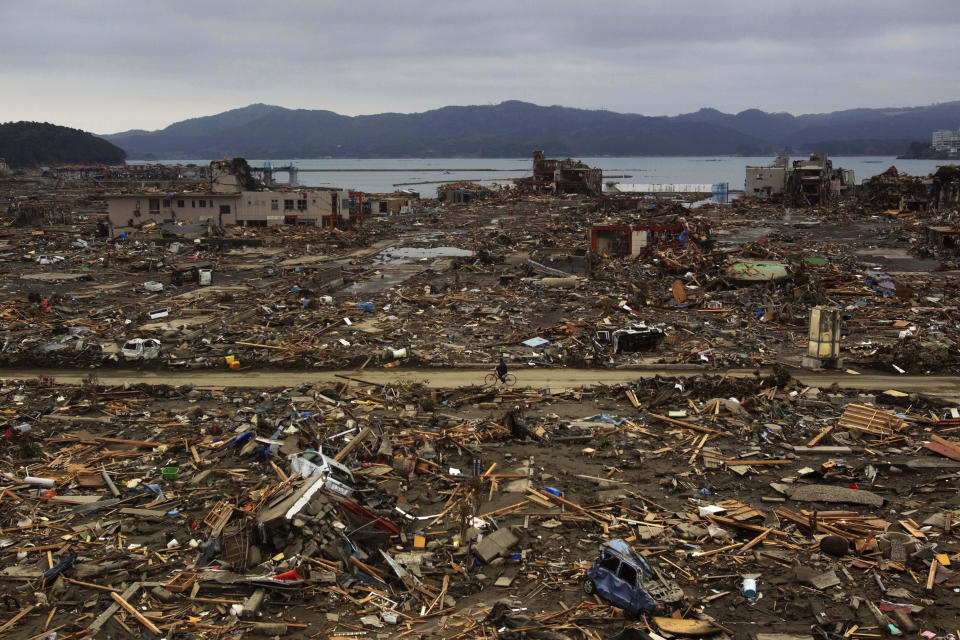 In this March 5, 2016, file photo, a survivor of the earthquake and tsunami rides his bicycle through the leveled city of Minamisanriku, in northeastern Japan, four days after the Tsunami. (AP Photo/David Guttenfelder, File)