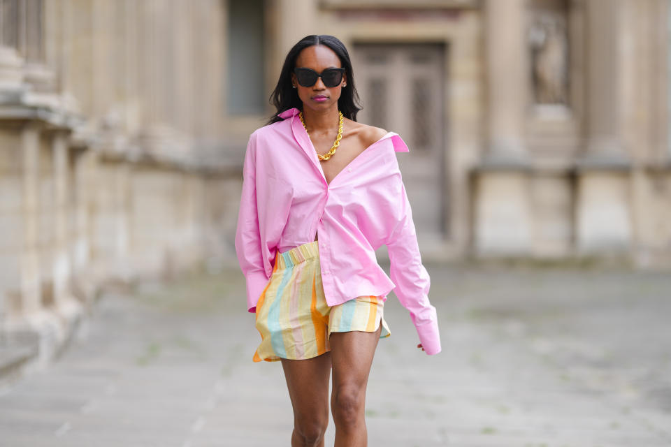 PARIS, FRANCE - JUNE 05: Emilie Joseph @in_fashionwetrust wears black sunglasses, silver earrings, a gold chunky necklace from Merbabe, a pale pink oversized boyfriend shirt worn off shoulder, a gold ring, large multicolor stripes pastel bower shorts, on June 05, 2021 in Paris, France. (Photo by Edward Berthelot/Getty Images)