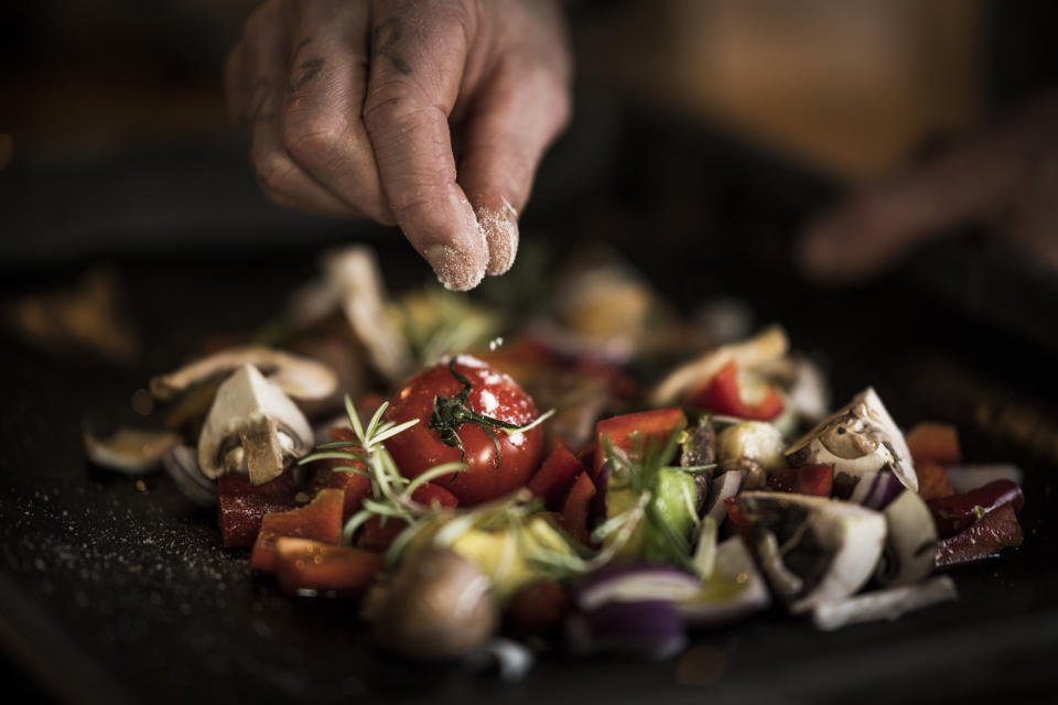 Hand seasoning vegetables on a baking sheet.